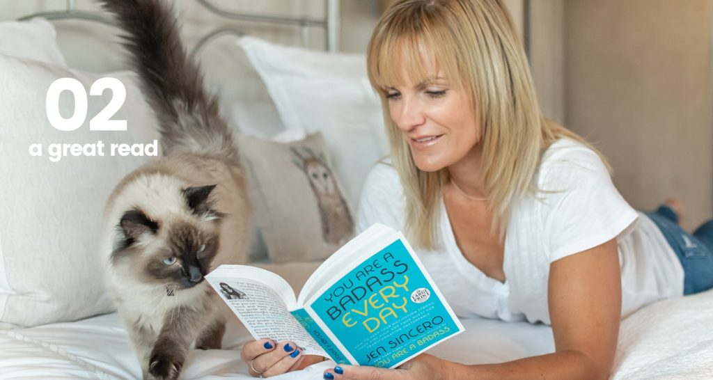 woman reading a book on her bed with a cat